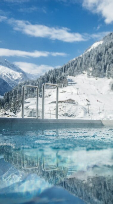 Außenpool mit warmem Wasser in verschneiter Berglandschaft, spiegelnder Himmel und Winteridylle. | © Max Steinbauer