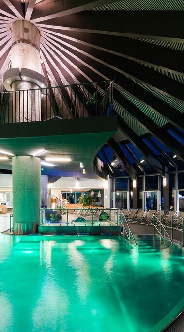 Modernes Hallenbad mit beleuchtetem Pool, Liegen und stilvoller Architektur am Abend. | © Kristallbad Wald - Königsleiten