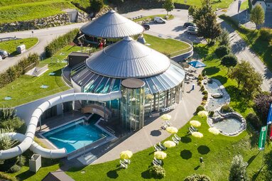 Luftaufnahme eines modernen Thermalbads mit Rutsche, Pool und grüner Außenanlage. | © Kristallbad Wald - Königsleiten
