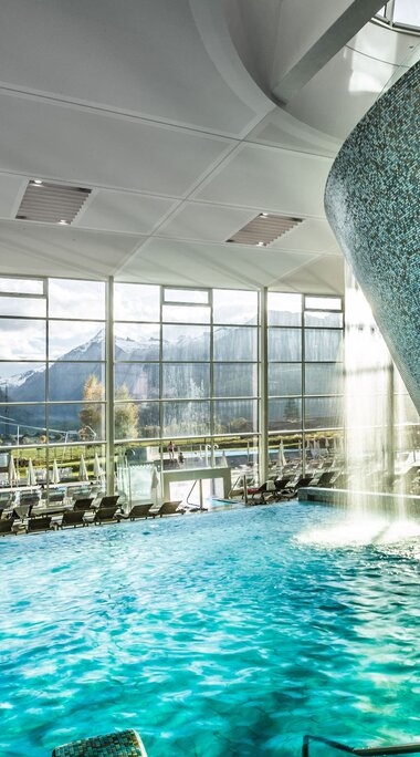 Innenpool mit Wasserfall und Panoramafenstern mit Blick auf die Berge. | © Ferienregion Nationalpark Hohe Tauern