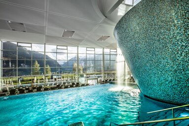 Innenpool mit Wasserfall und Panoramafenstern mit Blick auf die Berge. | © Ferienregion Nationalpark Hohe Tauern