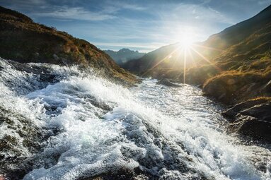 Fließender Bergbach im Sonnenlicht mit Blick auf Täler und Berge unter klarem Himmel Obersulzbachtal. | © Ferienregion Nationalpark Hohe Tauern - Daniel Breuer