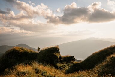 Person steht auf einer grünen Bergkuppe bei Sonnenuntergang mit weitem Blick über die Landschaft. | © Ferienregion Nationalpark Hohe Tauern - Gerald Demolsky