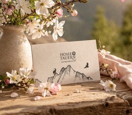 Nationalparkgutschein liegt auf Holztisch neben Frühlingsblumen und Blütenzweig | © Ferienregion NPHT - KI unterstützt