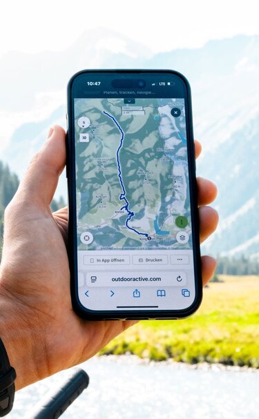 Smartphone zeigt Wanderroute vor alpiner Landschaft. | © Mathäus Gartner