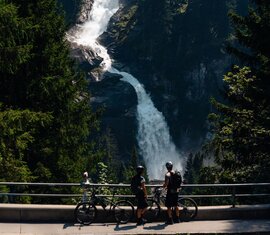 Mountainbiker stehen vor hohem Wasserfall im Wald. | © Mathäus Gartner