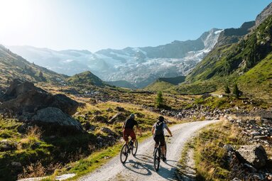 Zwei Mountainbiker fahren auf Schotterweg Richtung Gletscher. | © Mathäus Gartner