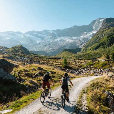 Zwei Mountainbiker fahren auf Schotterweg Richtung Gletscher. | © Mathäus Gartner