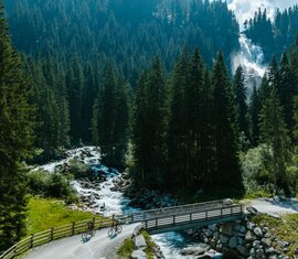 Zwei Radfahrer überqueren Brücke nahe Wasserfall im Wald | © Mathäus Gartner