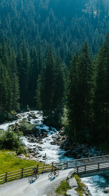 Zwei Radfahrer überqueren Brücke nahe Wasserfall im Wald | © Mathäus Gartner