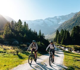 Two cyclists on a valley path with stream, forest and glacier in the background | © Mathäus Gartner