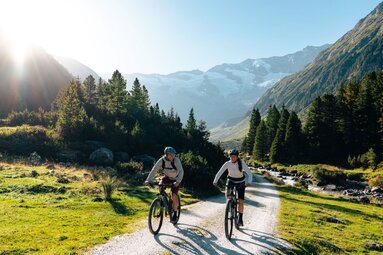 Zwei Radfahrer auf einem Talweg mit Bach, Wald und Gletscher im Hintergrund | © Mathäus Gartner