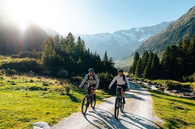 Zwei Radfahrer auf Schotterweg im sonnigen alpinen Tal. | © Mathäus Gartner