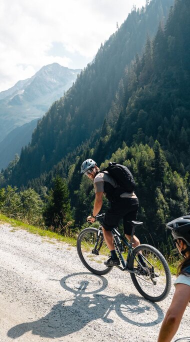 Zwei Mountainbiker fahren bergauf auf Schotterstraße im Tal. | © Mathäus Gartner