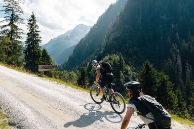 Zwei Mountainbiker fahren bergauf auf Schotterstraße im Tal. | © Mathäus Gartner