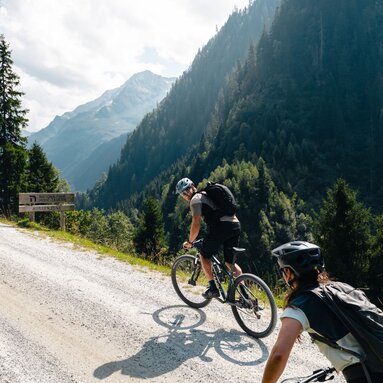 Two mountain bikers riding uphill on a gravel road in the valley. | © Mathäus Gartner