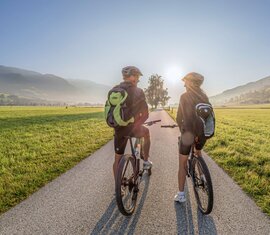 Zwei Radfahrer auf asphaltierter Strecke durch weite Wiesen im Morgenlicht. | © Lichtfarben