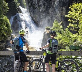 Zwei Mountainbiker stehen vor einem Wasserfall und betrachten die Schlucht | © WOM Medien GmbH - Andreas Meyer