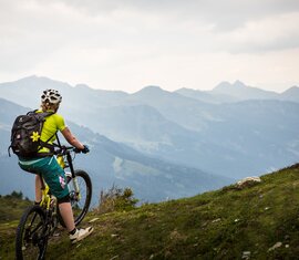 Mountainbiker hält auf einem Berggrat und blickt über ein weites Bergpanorama | © SalzburgerLand Tourismus