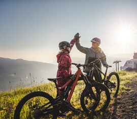 Zwei Mountainbiker haben auf einem Bergweg bei Sonnenaufgang mit ihren Bikes das Ziel erreicht | © Kitzsteinhorn