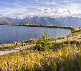 Zwei Radfahrer auf Weg entlang eines Bergsees mit Panorama auf Alpen und Gipfel | © Andreas Meyer WOM Medien - Mittersillplus