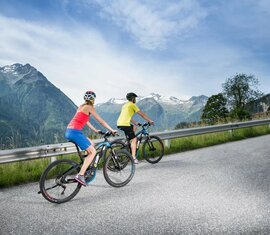 Zwei Radfahrer auf Bergstraße mit Blick auf Tal und schneebedeckte Gipfel | © Tourismusverband Wald-Königsleiten