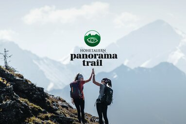 Zwei Wanderer geben sich High-Five vor Bergkulisse mit "Hohe Tauern Panorama Trail"-Logo. | © Ferienregion Nationalpark Hohe Tauern