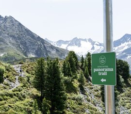 Hohe Tauern Panorama Trail sign in front of an alpine mountain landscape with hiking path. | © Hohe Tauern National Park holiday region - Jesus Tena