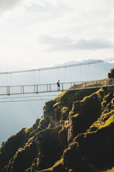Person crossing a suspension bridge in the mountains, overlooking a valley. | © Holiday Region National Park Hohe Tauern - Gerald Demolsky