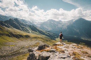Wanderer auf Bergplateau, blickt in ein weites Tal mit umliegenden Gipfeln und Wolken. | © Ferienregion Nationalpark Hohe Tauern - Gerald Demolsky