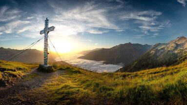 Gipfelkreuz auf Bergwiese mit Sonnenaufgang und Nebelmeer. | © Ferienregion Nationalpark Hohe Tauern / Florian Kreidl-Glueck