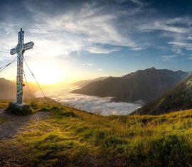 Summit cross on mountain meadow with sunrise and sea of clouds. | © Hohe Tauern National Park holiday region / Florian Kreidl-Glueck
