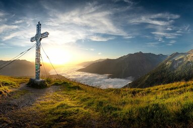 Summit cross on mountain meadow with sunrise and sea of clouds. | © Hohe Tauern National Park holiday region / Florian Kreidl-Glueck