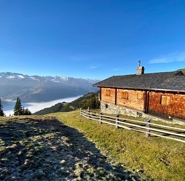 Eine Almhütte auf einer Wiese mit Blick auf ein nebelgefülltes Tal und schneebedeckte Berge. | © Tourismusverband Uttendorf/Weißsee