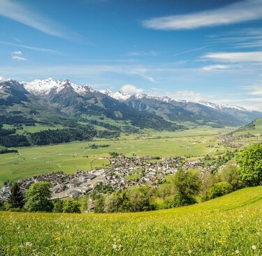 Panoramablick auf ein grünes Tal mit Dorf, umgeben von schneebedeckten Bergen und blauem Himmel. | © Tourismusverband Piesendorf Niedernsill - Harry Liebmann