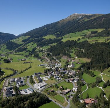 Luftaufnahme eines grünen Tals mit verstreuten Häusern und Wäldern, umgeben von Bergen. | © Zillertal Arena