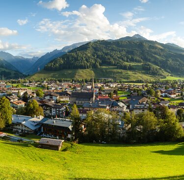 Panorama eines Dorfes inmitten eines grünen Tals, umgeben von bewaldeten Bergen bei Sonnenschein. | © Tourismusverband BRUCK FUSCH | GROSSGLOCKNER