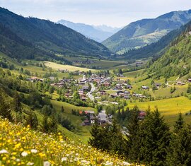 Blick auf ein idyllisches Dorf in einem grünen Tal, umgeben von Wiesen und bewaldeten Hügeln. | © BRUCK FUSCH | GROSSGLOCKNER - Sochor