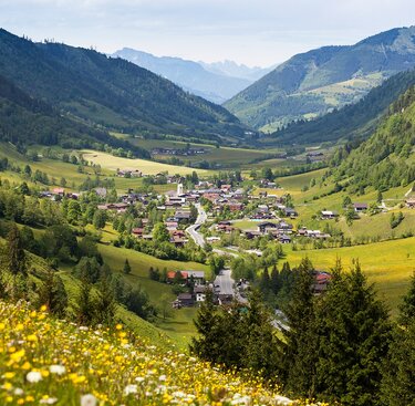 Blick auf ein idyllisches Dorf in einem grünen Tal, umgeben von Wiesen und bewaldeten Hügeln. | © BRUCK FUSCH | GROSSGLOCKNER - Sochor