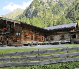 Traditionelle Almhütte mit Blumenbalkonen in idyllischer Berglandschaft. | © Ferienregion Nationalpark Hohe Tauern