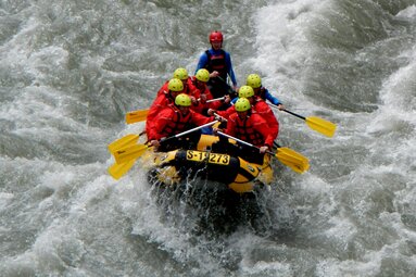 Rafting-Gruppe auf einem Fluss in einem Schlauchboot mit gelben Paddeln. | © FROST Rafting & Canyoning Tours