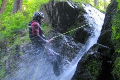 Eine Person seilt sich an einem Wasserfall ab, umgeben von dichtem Wald. | © Sports & more Unterwurzacher