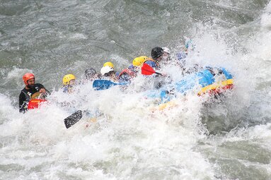 Gruppe von Menschen im Rafting-Boot, umgeben von spritzendem Wasser. | © Rafting Center Taxenbach