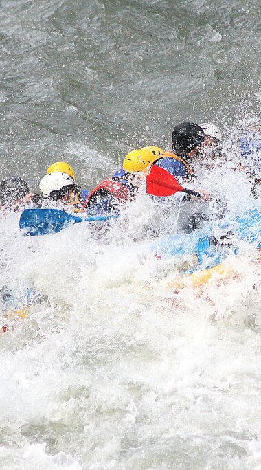Gruppe von Menschen im Rafting-Boot, umgeben von spritzendem Wasser. | © Rafting Center Taxenbach