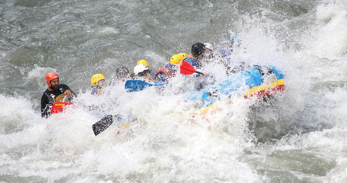 Gruppe von Menschen im Rafting-Boot, umgeben von spritzendem Wasser. | © Rafting Center Taxenbach