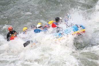 Gruppe von Menschen im Rafting-Boot, umgeben von spritzendem Wasser. | © Rafting Center Taxenbach