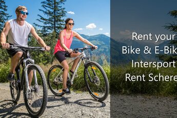 Paar fährt Mountainbikes auf einem sonnigen Weg mit Bergblick. | © Intersport Scherer