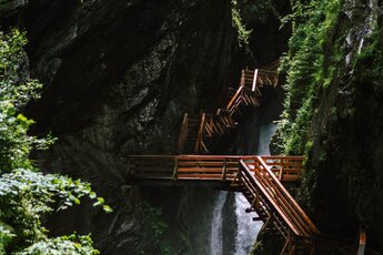 Holzstege und Treppen in der Sigmund-Thun-Klamm mit Wasserfall zwischen Felswänden. | © Sigmund Thun Klamm Kaprun