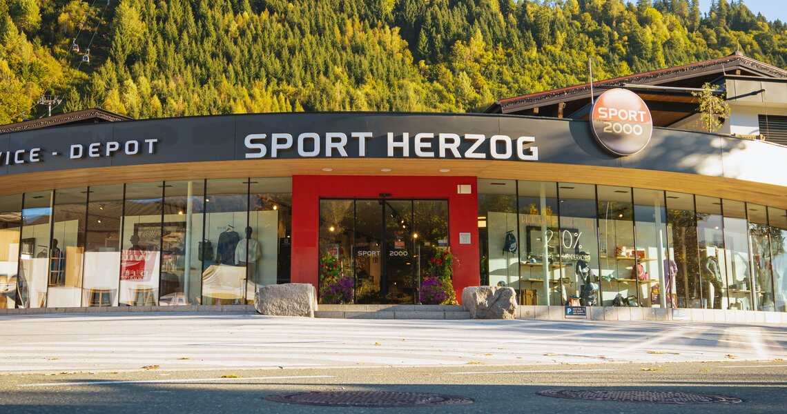 Sportgeschäft Sport Herzog mit großer Glasfront vor bewaldetem Berghang. | © Sport 2000 Herzog
