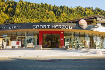 Sportgeschäft Sport Herzog mit großer Glasfront vor bewaldetem Berghang. | © Sport 2000 Herzog